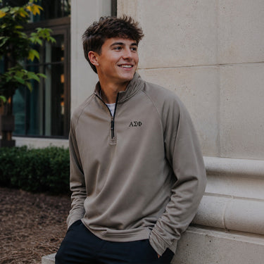 College-aged man wearing the Mushroom Cutter & Buck Adapt quarter-zip with black embroidered Alpha Sigma Phi Greek letters outdoors on campus.