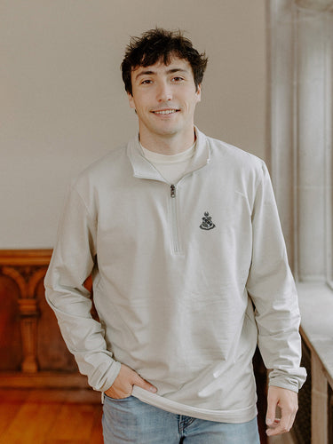 Male model wearing the smoke-colored Alpha Sigma Phi Embroidered Luxe Quarter Zip with crest embroidery, standing by a window in a formal setting.