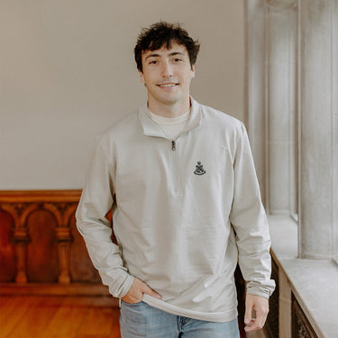 Male model wearing the smoke-colored Alpha Sigma Phi Embroidered Luxe Quarter Zip with crest embroidery, standing by a window in a formal setting.