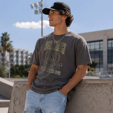 College-aged male wearing the fraternity Collegiate Crest Graphic Tee in charcoal grey, featuring vintage Alpha Sigma Phi crest artwork on campus.