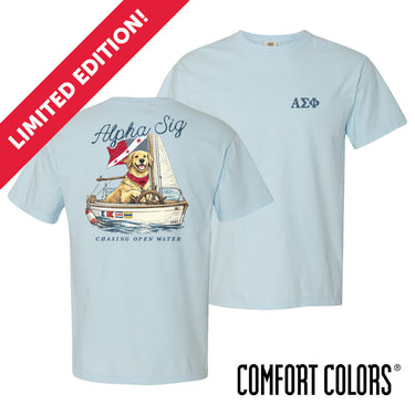 Light blue Comfort Colors t-shirt shown front and back; front features small Greek letters on the left chest, back displays a golden retriever sailing a boat with script text above and “Chasing Open Water” below.